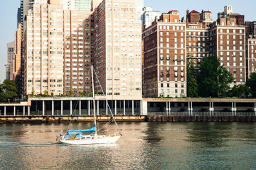 View of midtown Manhattan skyline and sailboat that is cruising on East River during sunny summer day