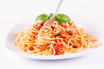 Spaghetti bolognese eaten with a fork decorated with basil on a white background