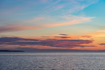 Evening sunlight on coast, pink clouds, blue sky reflection on water. Beach in summer. Seaside natural environment. Shore in Harilaid, small island in Estonia. Nature Reserve in North Europe