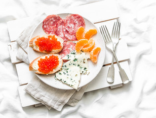 Breakfast in bed - red caviar sandwiches, blue cheese, salami, tangerines on a light background, top view. Flat lay, copy space