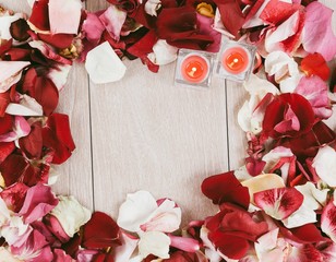 two candles in a frame of rose petals on a wooden background