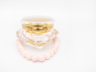 Skin care cream in a beautiful diamond shaped glass jar packaging with a perl necklace isolated on a white background