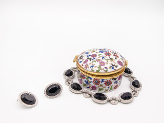 Beautifully ornamented porcelain jewelry box with a floral motive and a vintage flair, with a silver bracelet and earrings and beautiful black gems isolated on a white background