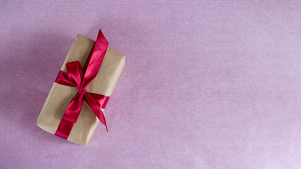 on a pink background is a gift box wrapped in Kraft paper and tied with a red satin ribbon...