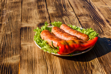 Ceramic plate with grilled sausages, pepper and lettuce leaves on wooden table