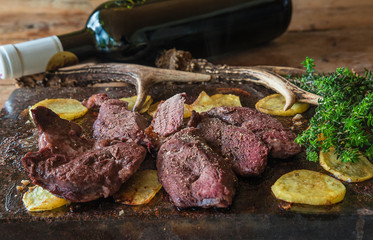 Deer steak and potatoes roasted on a slate, bottle of red wine and deer antlers close up