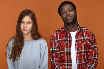 Picture of young couple having sad unhappy looks after sleepless night because of their baby child crying, posing isolated in studio. Interracial love, relationships and togetherness concept