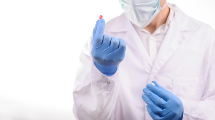 a doctor with mask in a white uniform looking at a red capsule that he is holding in his hand in a blue glove