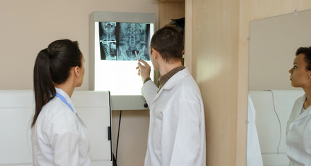 Obraz premium Back view: picture of two doctors exploring spinal x-ray: lumbar and cervical region - first 2 cervical vertebrae (axis and atlas), coxofemural joint