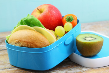 Healthy school lunch box containing cheese roll, crunchy yellow pepper and fresh fruit: grapes, apple and kiwi fruit
