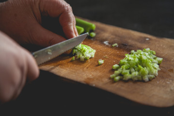 Woman preparing food in her kitchen, she is chopping fresh celery on a cutting board with a knife on the tray