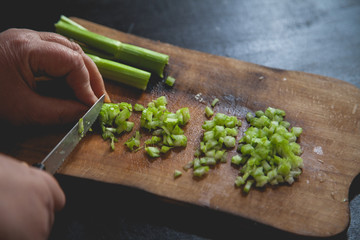 Woman preparing food in her kitchen, she is chopping fresh celery on a cutting board with a knife on the tray