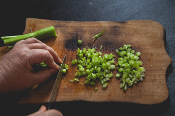 Woman preparing food in her kitchen, she is chopping fresh celery on a cutting board with a knife on the tray