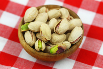 Pistachio nuts with and without shell in mini bamboo bowl on red and white checkered cloth, closeup
