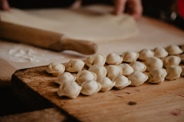 Uncooked russian pelmeni on cutting board and ingredients for homemade pelmeni on white table. Process of making pelmeni, ravioli or dumplings with meat