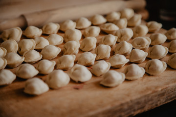 Uncooked russian pelmeni on cutting board and ingredients for homemade pelmeni on white table. Process of making pelmeni, ravioli or dumplings with meat
