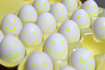 Group of eggs with drawn emotions. White chicken eggs in a cardboard package, with cartoon faces. background, texture