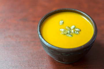 Pumpkin cream-soup with addition of pumpkin seeds and spices, view from above, studio shot. Clay plate of pumpkin cream-soup with addition of pumpkin seeds and spices, above view. copy space.