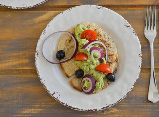Healthy breakfast. Avocado salad with sherry tomatoes olives and onion on pita bread. On wooden table.