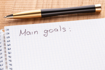 Top view workplace notebook and pen on wood table background, retro effect. The inscription - main oals.