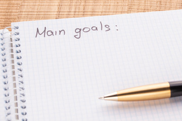 Top view workplace notebook and pen on wood table background, retro effect. The inscription - main oals.
