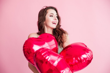 Happy young woman with red balloons smilling over pink background.