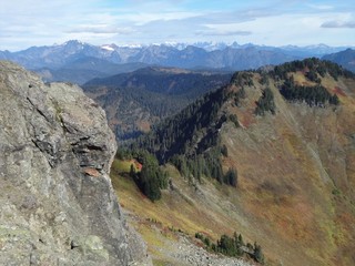 Fall colors cover the slope of a mountain with the rugged peaks of the North Cascades