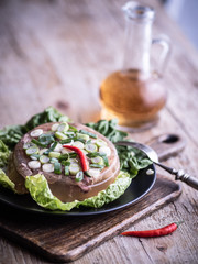 Homemade jelly meat with chilli pepper, green salad and bottle of vinegar on wooden table.