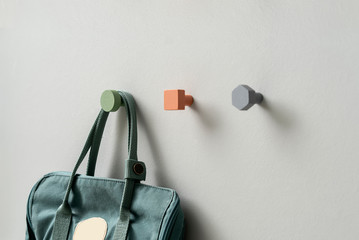 Metal multicolored geometric hangers with hanging casual bag on light wall in studio