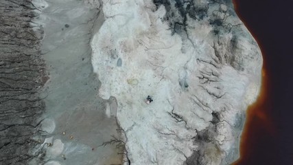 Aerial view of beautiful couple in fancy dresses of princess and robot embrace on grey rocky surface near the pond with brown water. Footage. Movie characters