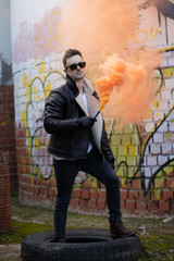 Man with modern clothes and sunglasses with an orange smoke flare in an abandoned place