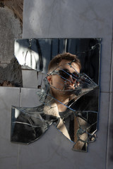 Reflection of boy with sunglasses in a broken mirror