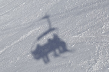 On the snow slope of the ski piste, the shadow of the skiers is displayed, which climb the lift