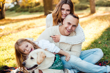Fototapeta na wymiar Happy beautiful family with dog labrador is having fun are sitting on green grass in park.