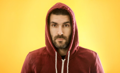 Portrait of handsome bearded man in a red hoodie against the yellow background