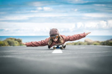 Beautiful child lying skateboard flies vintage pilot suit with hat leather jacket and mask takes...