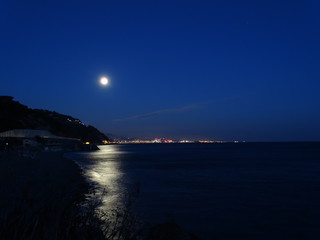 Fototapeta premium luna piena che si specchia nel mare sopra le luci del porto