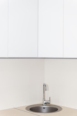 New modern faucet and kitchen room sink closeup with round stainless steel basin and countertop in model house home apartment and white vertical countertops