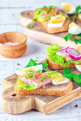 Sandwich with herring and tuna fillets with fresh green salad, onion ring, a quarter of eggs, home cheese, piece of lemon, micro greens and scallions on the wooden desk