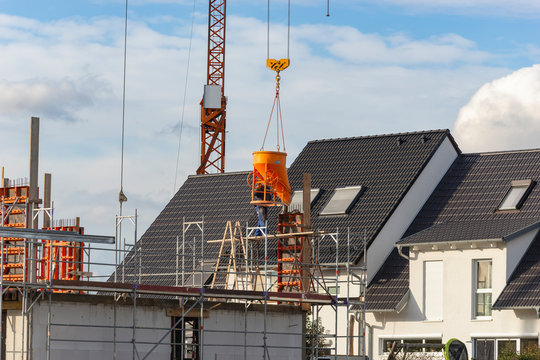 Baustelle mit Bauarbeitern und Kran an dem ein Betonk&uuml;bel h&auml;ngt.