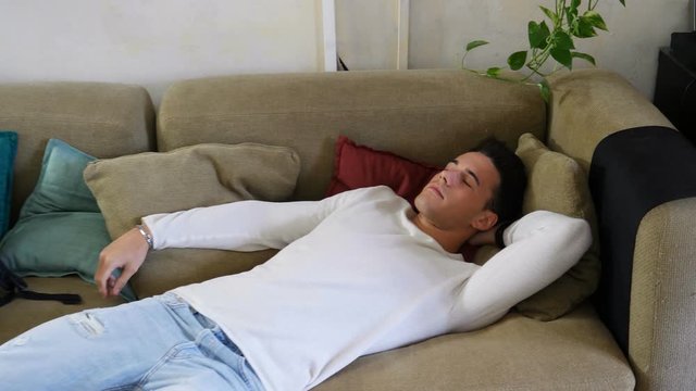 Young man arriving at home and falling on couch because he's very tired