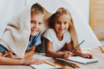 Happy kids drawing together covering by blanket