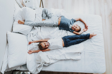Joyful brother and sister laying on bed and have fun