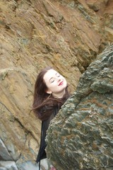 Long haired brunette girl hides behind a rock on a beach