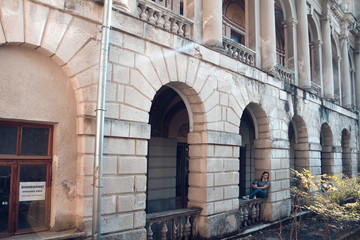 young woman sitting on the window of an old abandoned building with columns