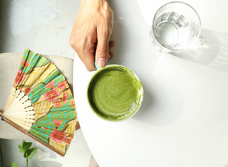 Hands holding a cup of green matcha latte coffee on white table background. Top view