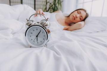 Alarm clock locating in front of young woman on bed