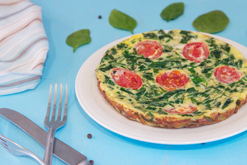 Spinach frittata ,italian omelet with cherry tomatoes in a white plate on a blue background. Healthy food conception