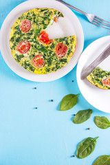 Spinach frittata ,italian omelet with cherry tomatoes in a white plate on a blue background. Healthy food conception