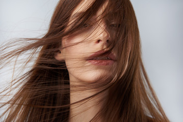 Young lady with hair strands on her face posing against light blue background